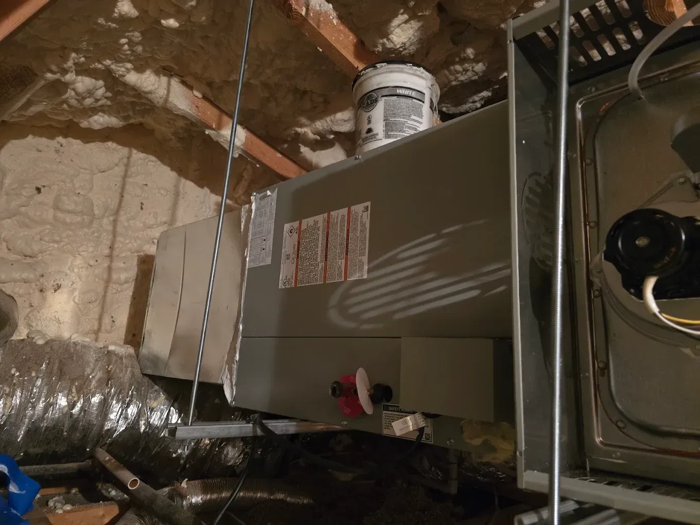 Basement HVAC unit and exposed ductwork against unfinished ceiling and walls.