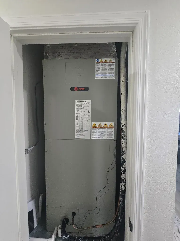 Tall gray HVAC unit in a closet with white walls and safety labels.