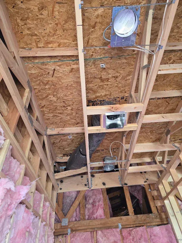 Unfinished attic ceiling framing with exposed wood trusses, insulation, and recessed light fixtures.