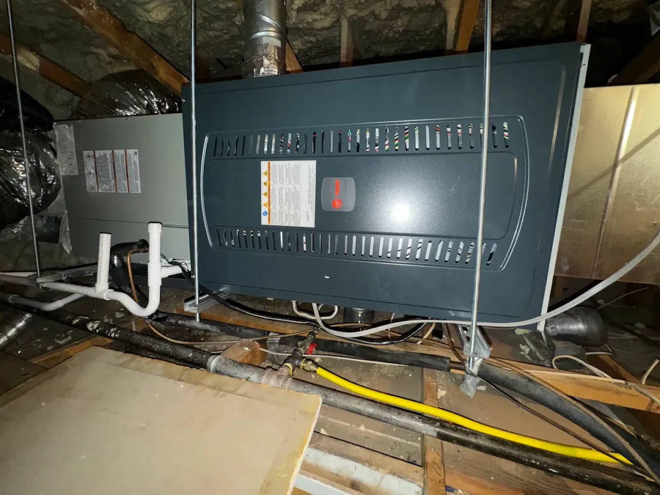 Electrical equipment and wiring in a dusty attic, with two gray control panels mounted on wooden beams.