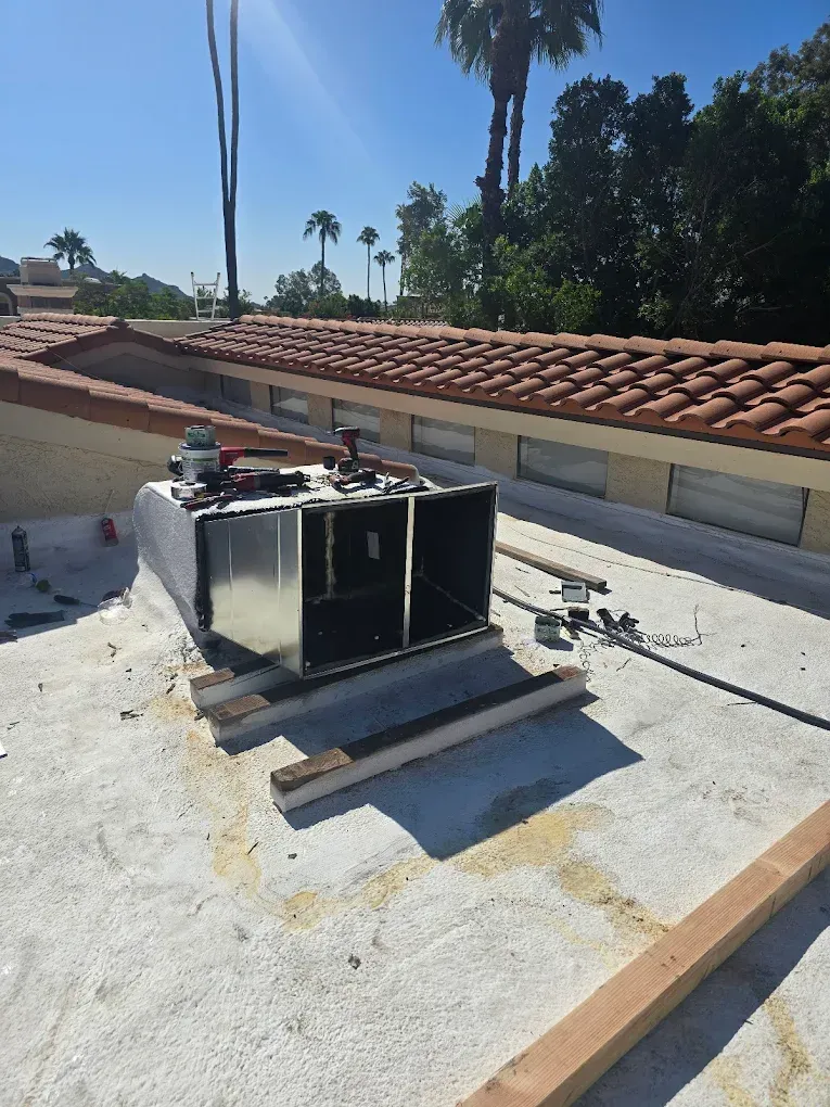 Rooftop HVAC unit on a flat roof beside a red tile parapet, with tools and debris nearby.