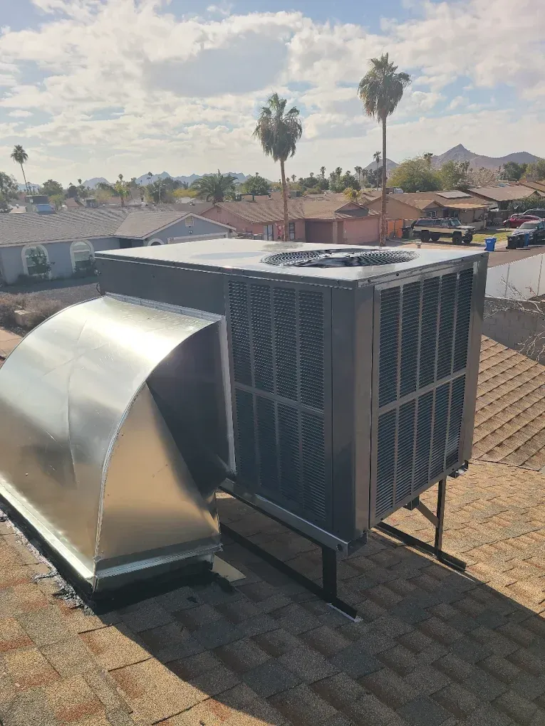 Rooftop HVAC unit with metal ducting under a sunny sky, with palm trees and houses in the background