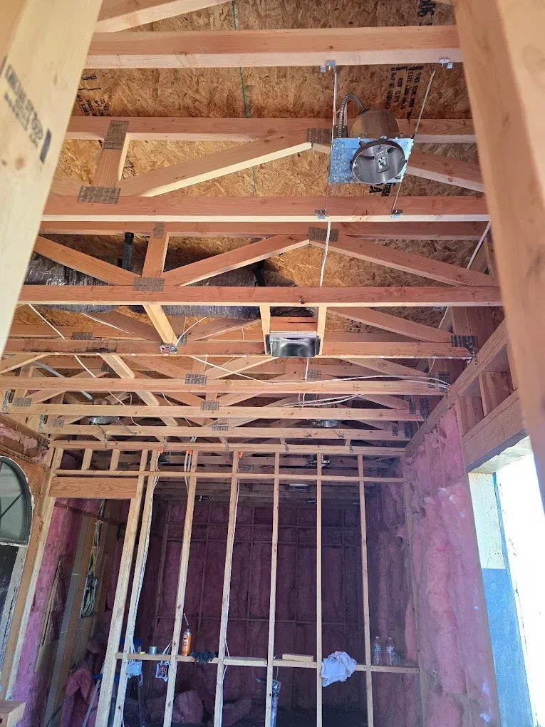 Unfinished room with exposed wooden ceiling trusses, open wall framing, and a hanging light fixture.
