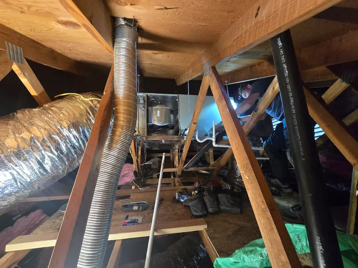 Crawlspace under a house with exposed beams, insulation ducting, and a small HVAC unit