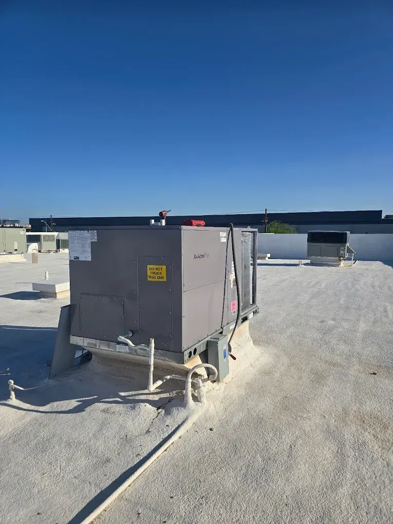 Gray rooftop HVAC unit on a gravel roof under a clear blue sky.