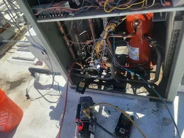 Open electrical equipment cabinet with tangled wires and a red fire extinguisher inside, on a concrete floor