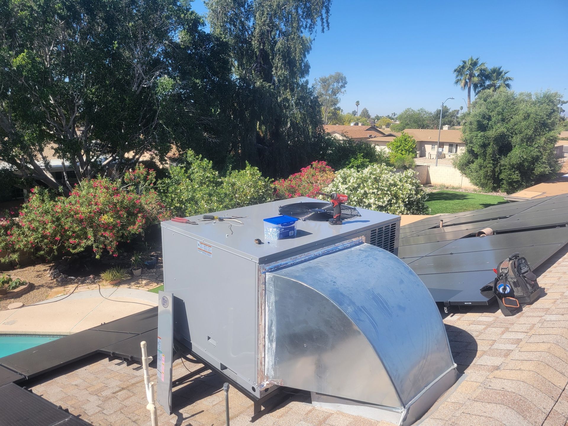 Metal rooftop HVAC unit on a paved patio, with trees and houses in the background.