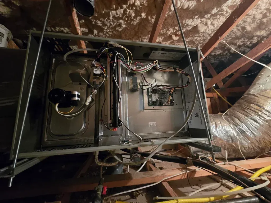 Open HVAC air handler in attic with exposed wiring, ducts, and metal components