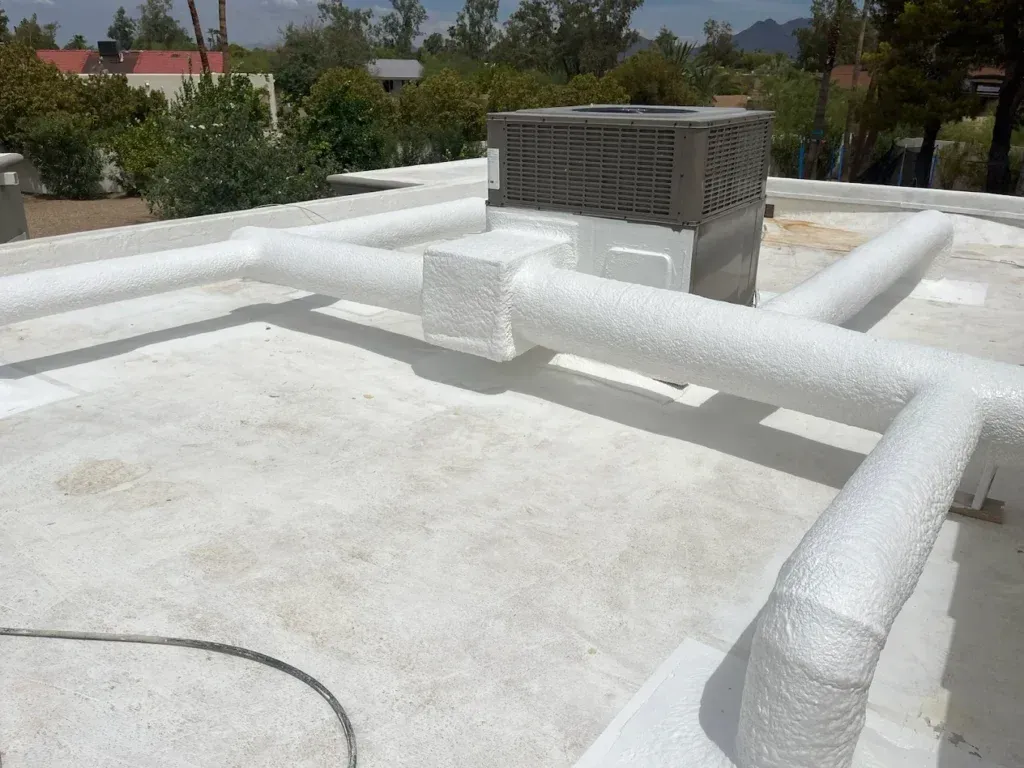 White insulated rooftop ducts and a metal HVAC unit on a flat roof under a clear sky