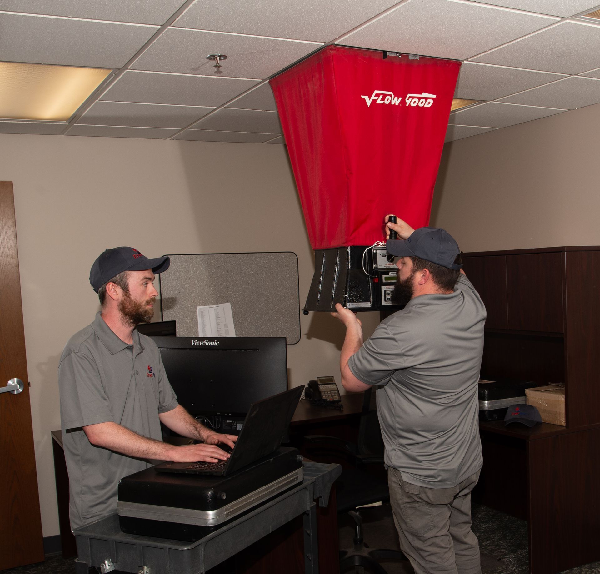 Two men are working in a room with a red bag that says