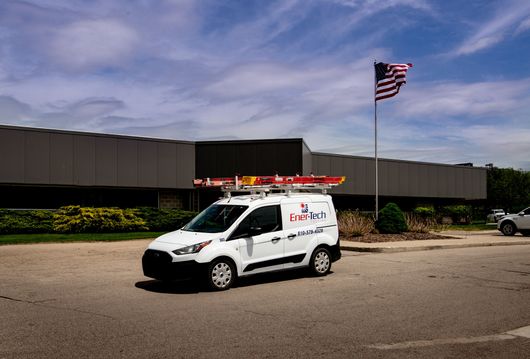 A white van is parked in front of a building with an american flag in the background.
