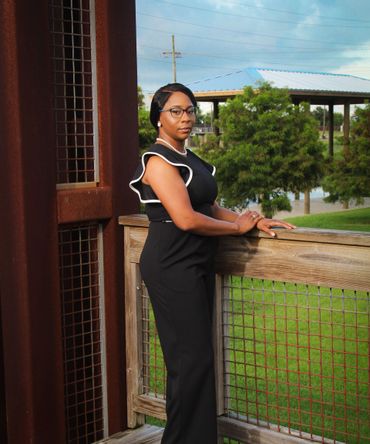 A woman in a black jumpsuit is leaning against a wooden railing.