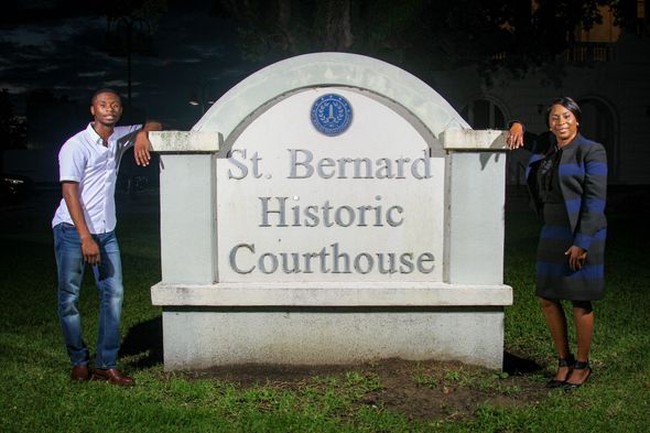 A man and a woman are standing next to a large stone sign that says st. bernard historic courthouse.