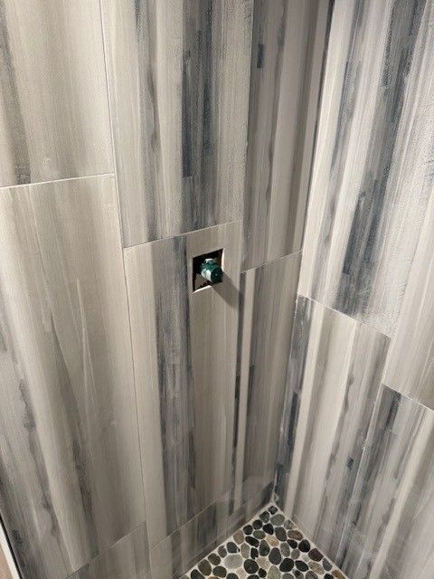 Tiled shower corner with a chrome shower control and pebble mosaic floor trim