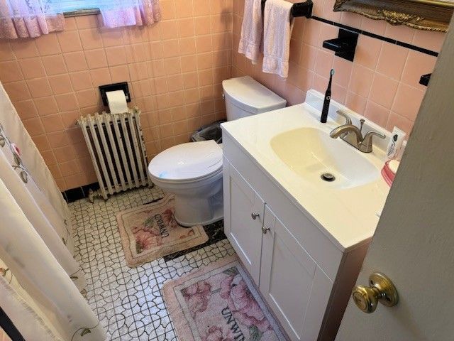 Small pink bathroom with toilet, sink vanity, radiator, tiled floor, and shower curtain.