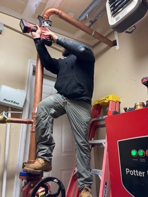 owner of steen & son plumbing and heating standing on a ladder using a drill to assemble a commercial 3 inch line