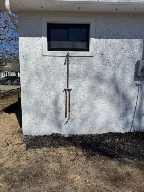 a white exterior wall of a house with window and copper pipes for an outdoor shower