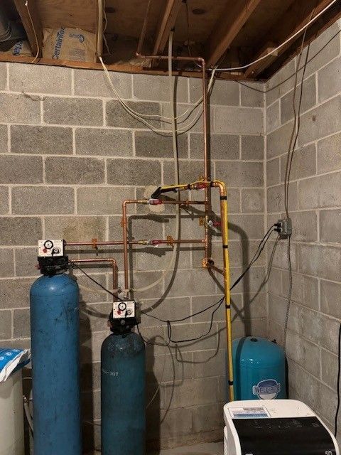 Basement utility room with water softeners, pipes, and tanks against cinder block walls