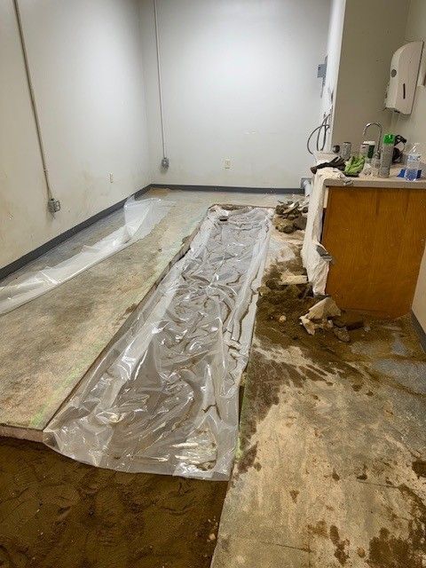 Flood-damaged room with wet floor, plastic sheeting, and debris near a countertop