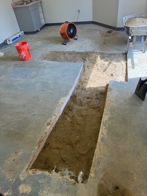 Indoor room with a long rectangular trench cut into the concrete floor, tools nearby.