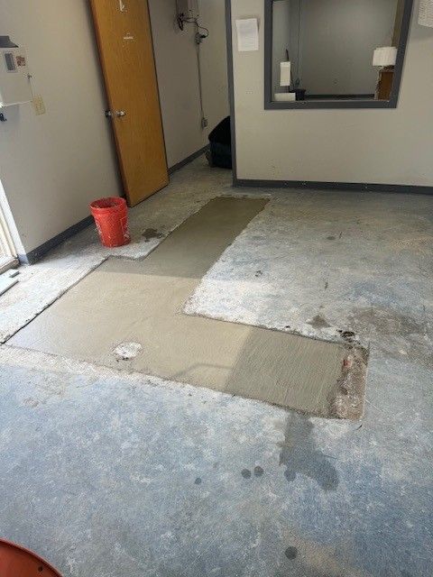 Partially removed carpet exposing concrete floor in an office hallway, with a red bucket near the wall
