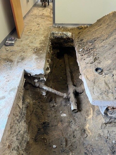 Open floor trench with exposed pipes in a damaged indoor hallway