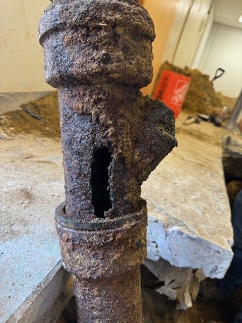 Rusty damaged metal valve with a large side hole, sitting on a workbench in a workshop.