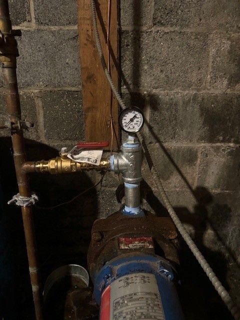 Pressure gauge and valves on a blue pipe in a basement utility area against a concrete wall