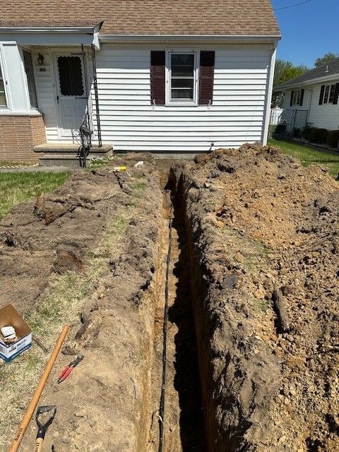 House exterior with a long trench dug beside the foundation and a shovel in the dirt.