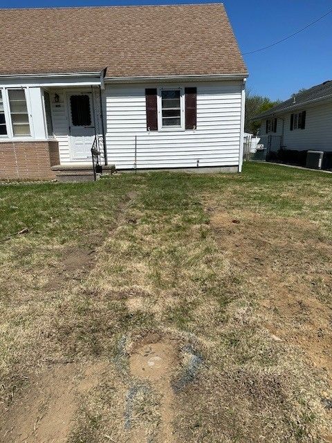 Front yard with patchy brown grass beside a white house under a clear blue sky.