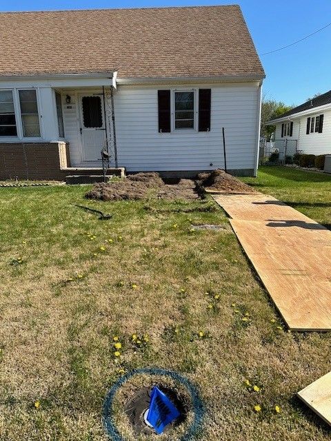 Front yard of a house with a plywood walkway and exposed utility area near the foundation