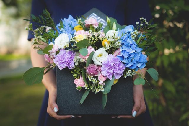 Person holding a box of colorful flowers outdoors