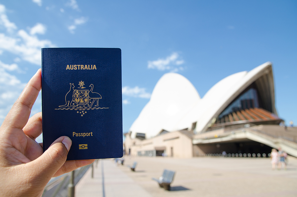 Uma pessoa está segurando um passaporte em frente à ópera em Sydney.