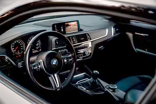 BMW car interior with black leather seats, steering wheel, dashboard display, and center console