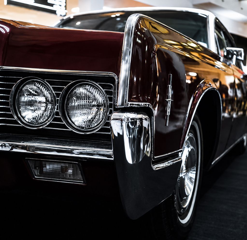 Close-up of a black vintage luxury car with chrome trim and dual round headlights indoors