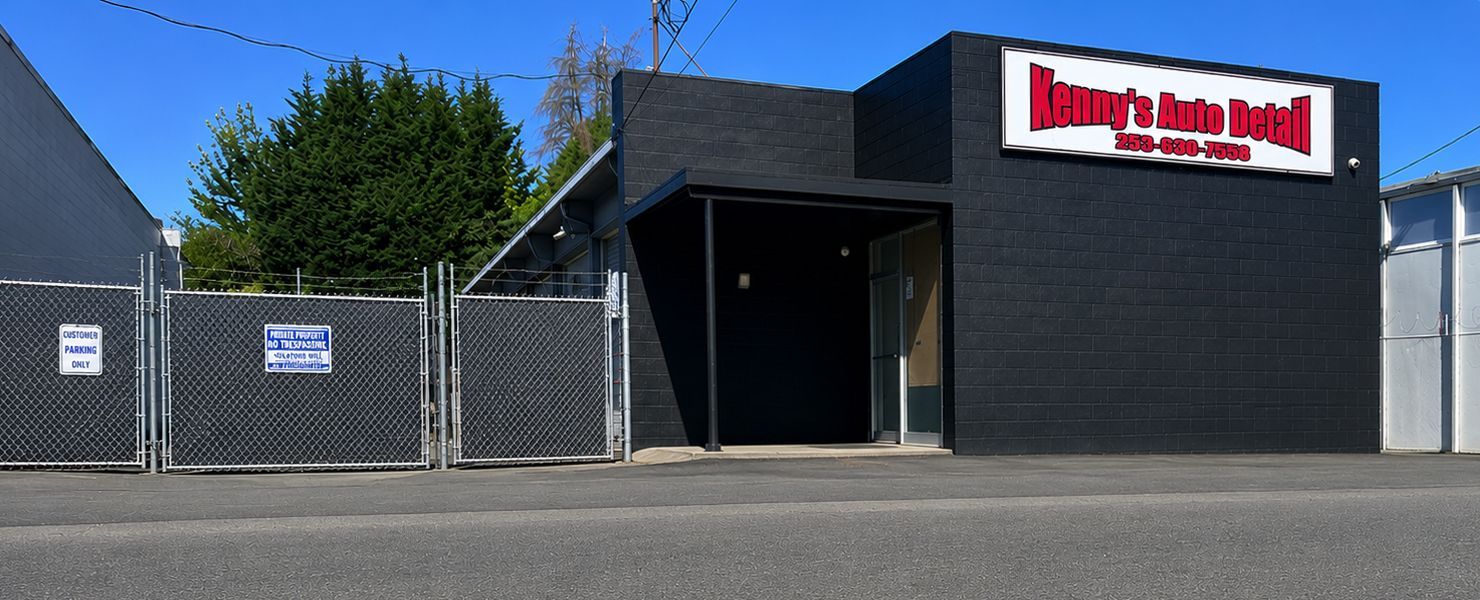 Exterior view of an auto repair shop with red trim, and three garage bays. Cars are parked inside.