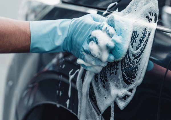 A person is washing a car with a sponge and soap.