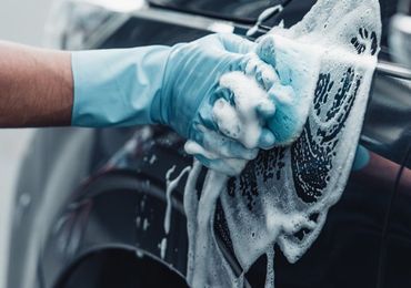 A person is washing a car with a sponge and soap.