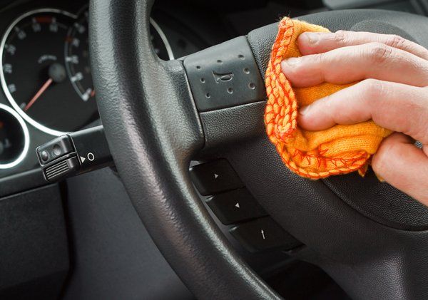 A person is cleaning the steering wheel of a car with a cloth.