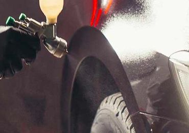 A person is spraying paint on the fender of a car.
