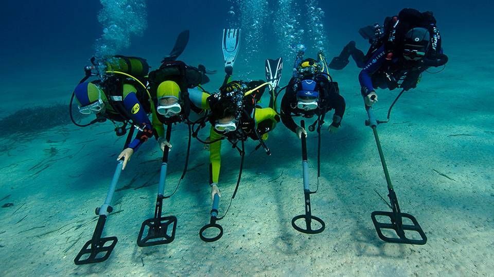 Een groep duikers gebruikt metaaldetectoren onder water.