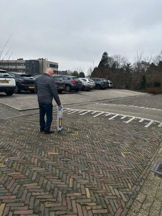 Een man staat op een parkeerplaats met een tas in zijn handen.