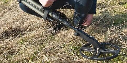 Iemand knielt in het gras en gebruikt een metaaldetector.