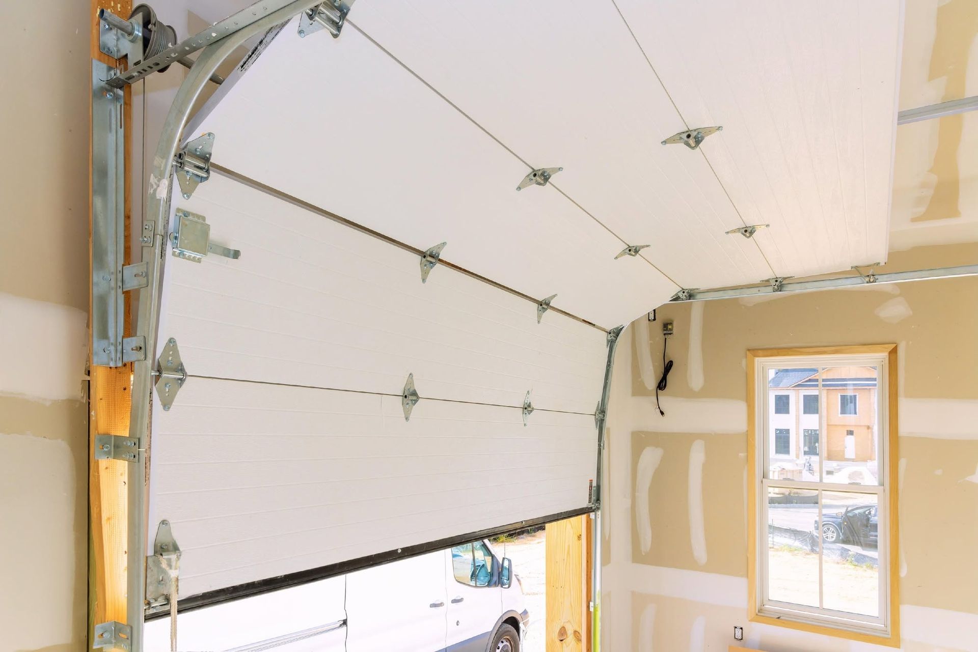 Open garage door with white panels and a small window, viewed from inside a partially finished room.