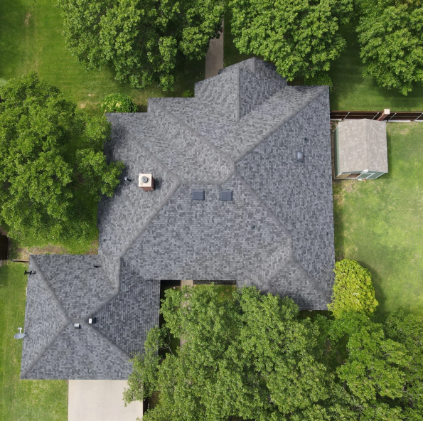 An aerial view of a house with a roof surrounded by trees and grass.