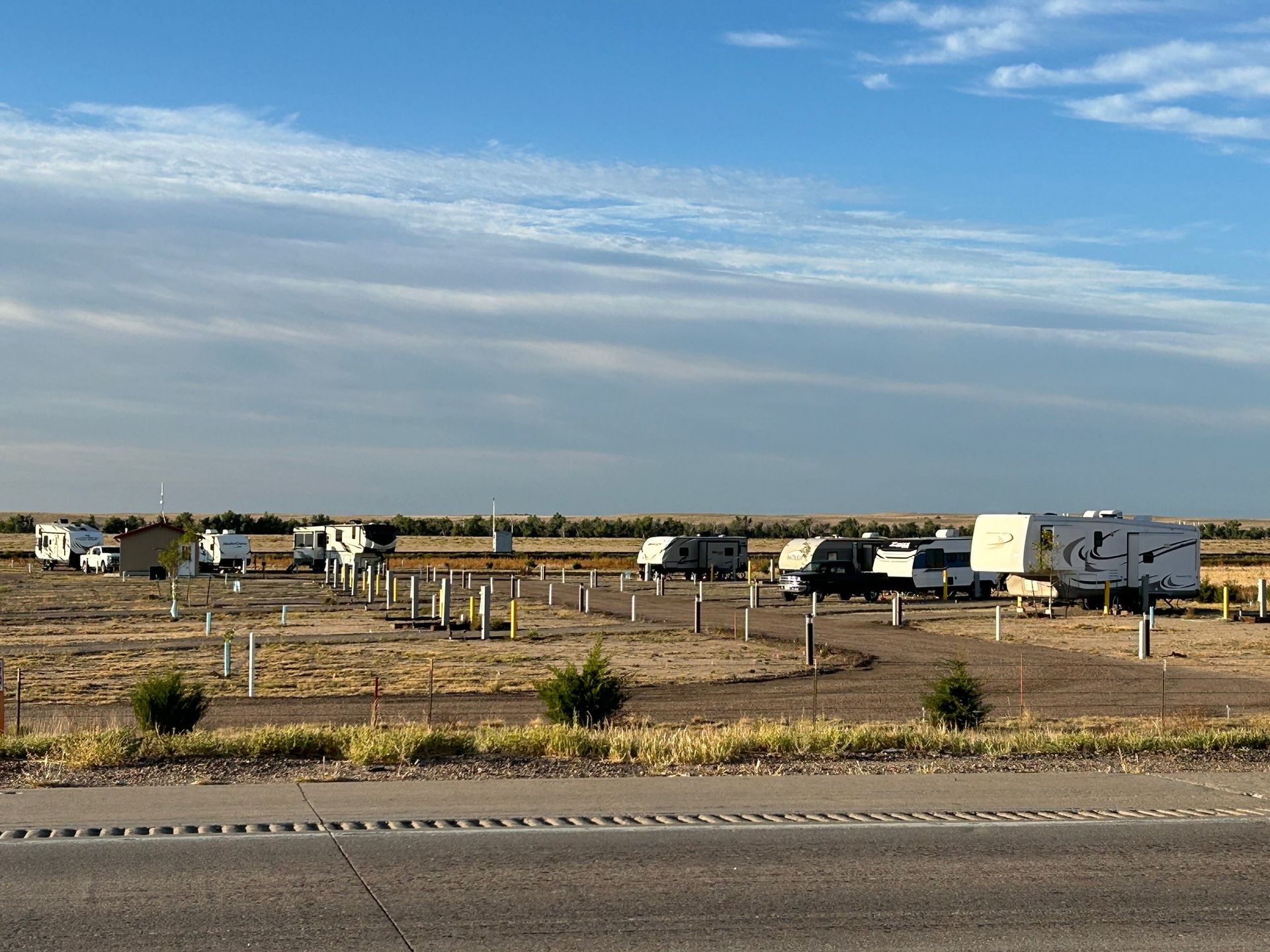 A row of rvs are parked in a field next to a highway.
