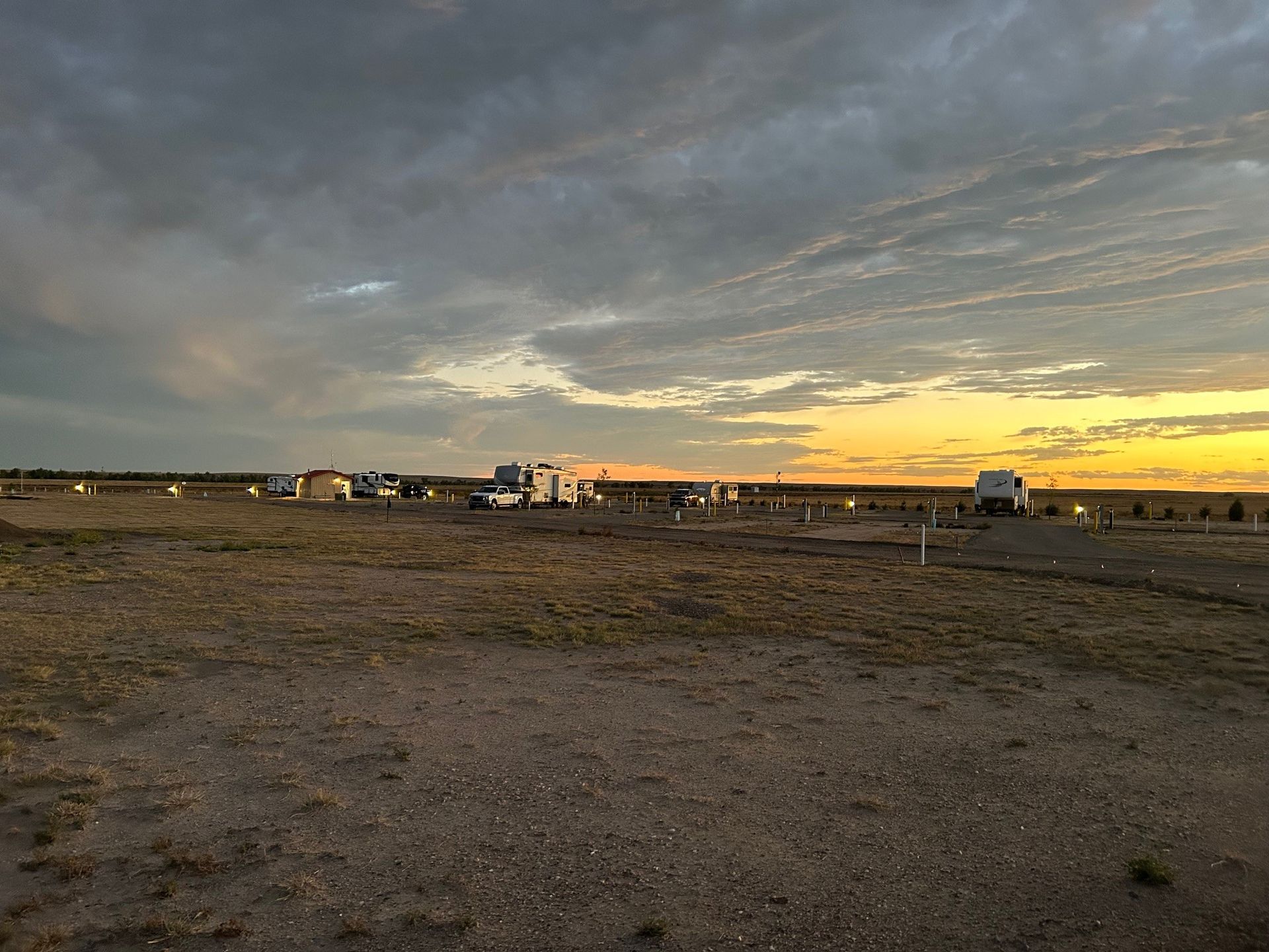 A group of rvs are parked in a field at sunset.
