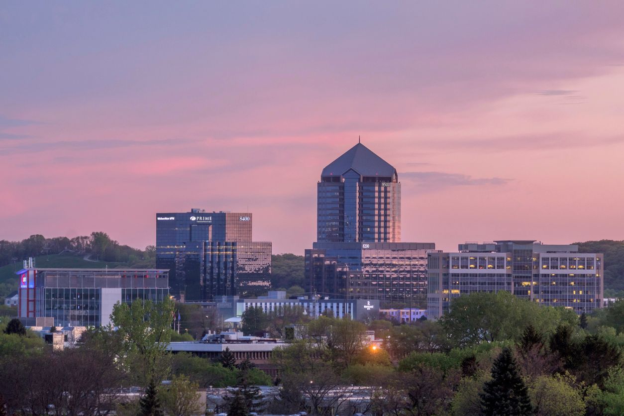A view of a city skyline with a tall, distinct pyramidal-topped building at dusk under a purple and pink sunset sky.