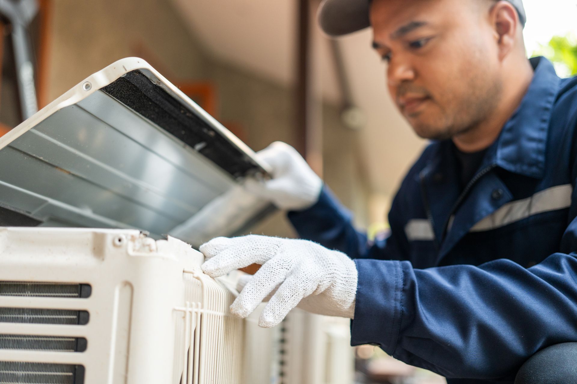 A technician in a blue uniform and gloves opens the top cover of an outdoor air conditioning unit to perform maintenance.