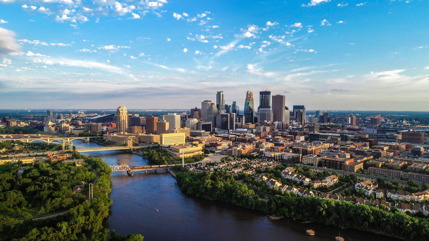 Aerial view of the Minneapolis skyline and the Mississippi River during sunset, with lush trees lining the riverbanks.